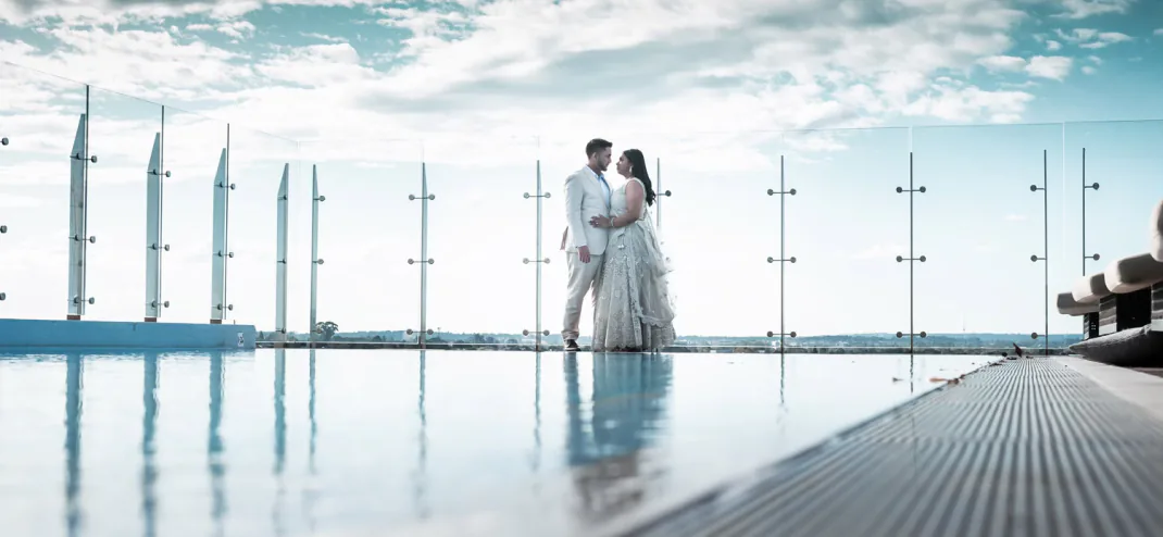 Bride and groom standing by a rooftop pool against the sky
