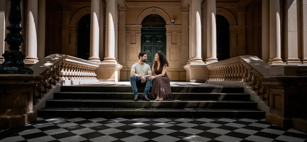 Couple sitting on sandstone steps in a colonnade with a chequered floor