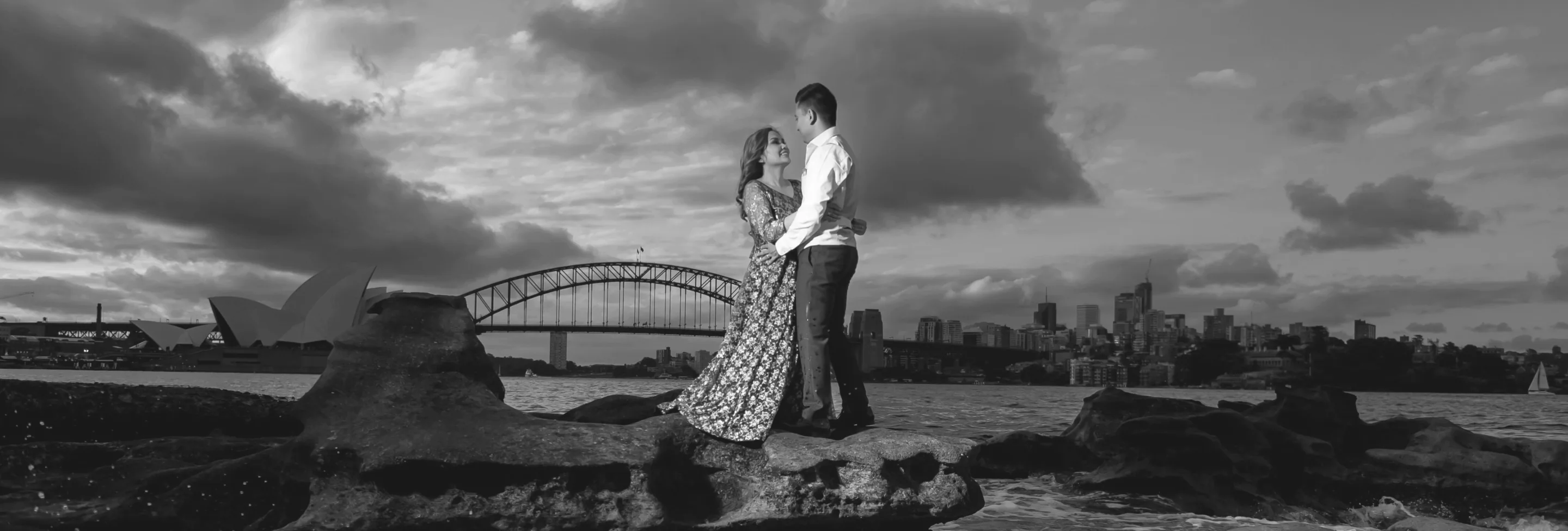 Couple on harbour rocks with the Sydney Opera House and Harbour Bridge behind them