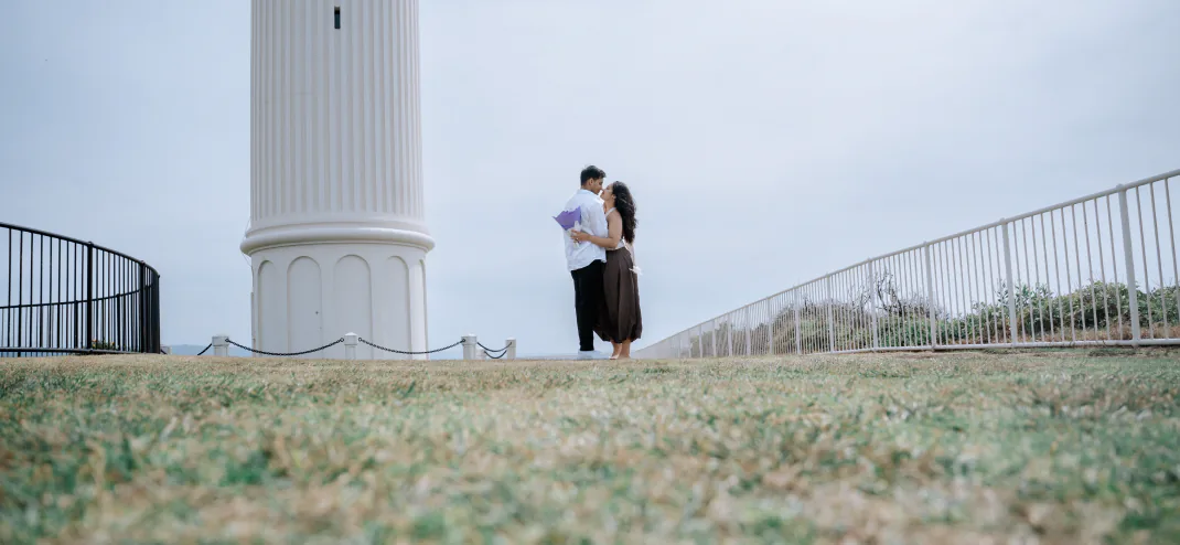 Couple embracing beside a white lighthouse during a pre-wedding shoot