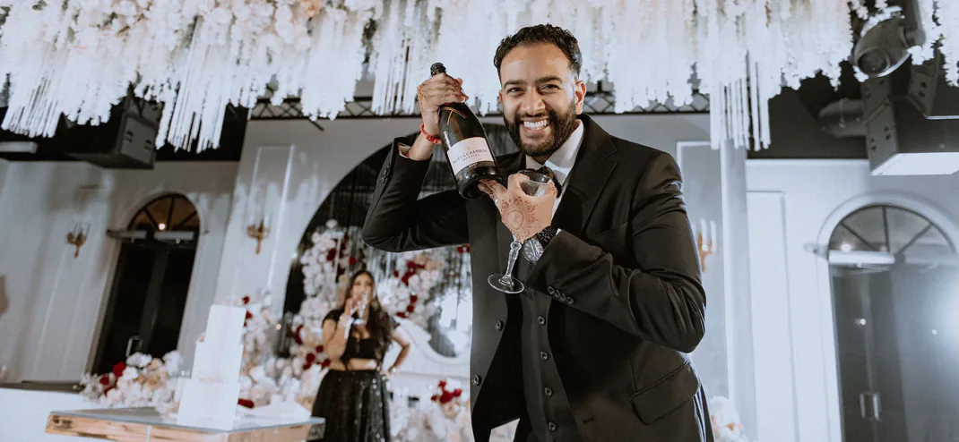 Groom opening champagne at a reception with white floral décor